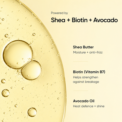 A close-up of a golden yellow shea butter oil with visible air bubbles on a cream background, with text reading 'Powered by Shea + Biotin + Avocado' and ingredient callouts for Shea Butter, Biotin (Vitamin B7), and Avocado Oil.